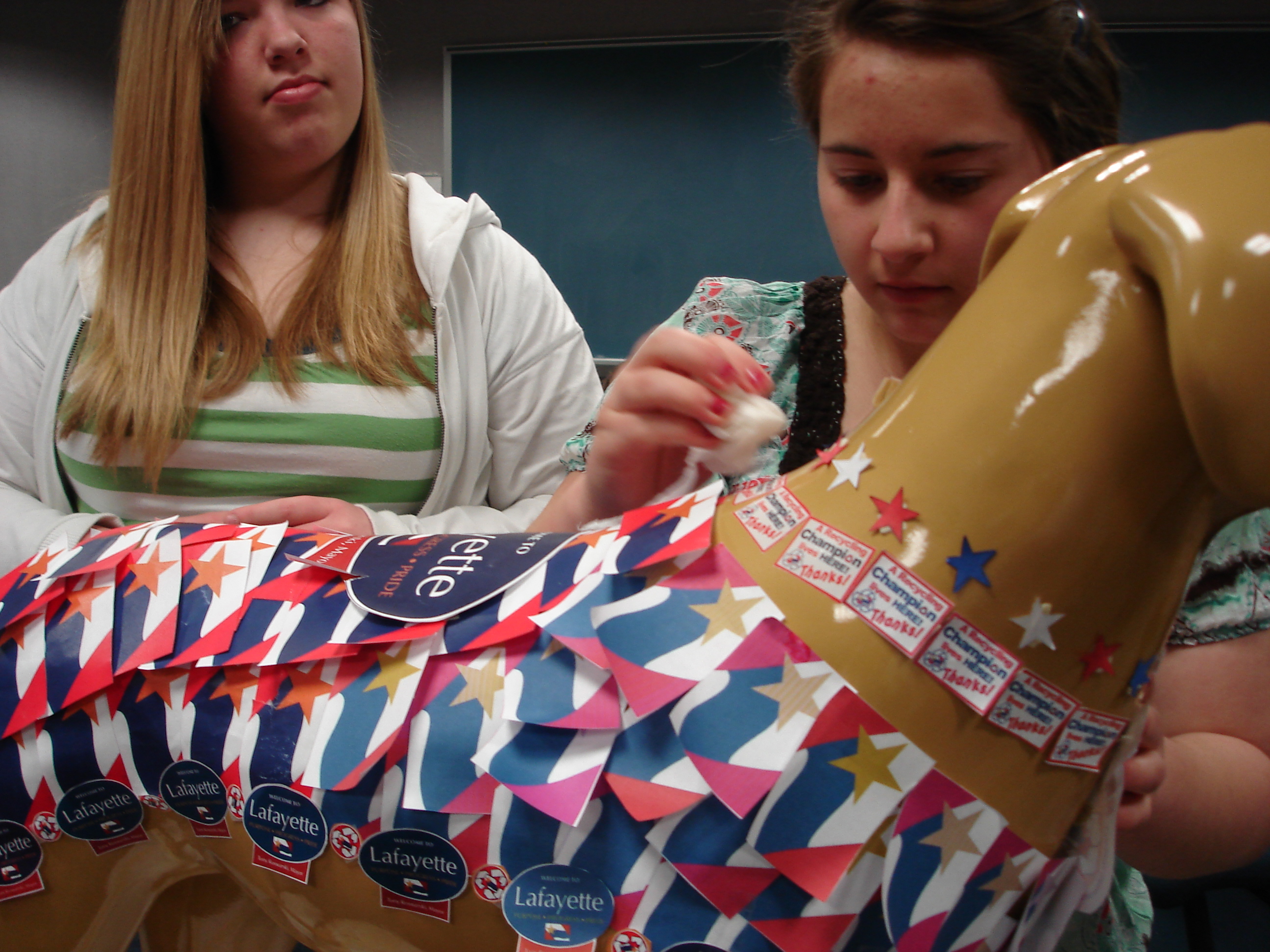 2 girls putting red, white and blue stickers on a plastic dog